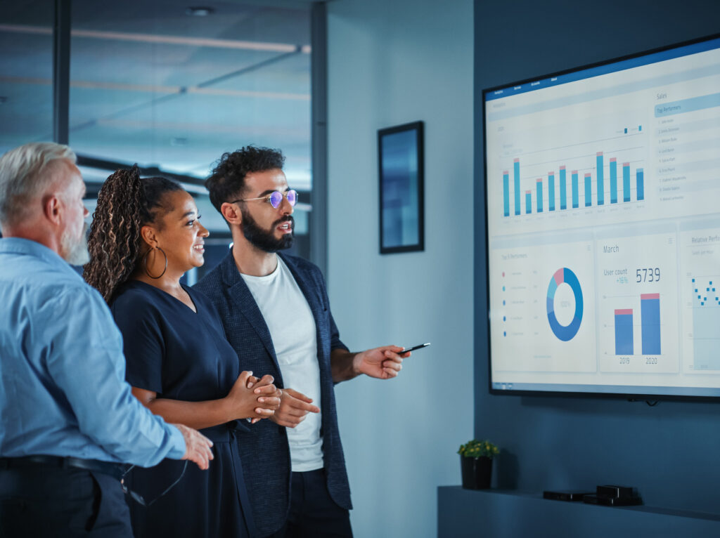 Company Operations Manager Holds Meeting Presentation. Diverse Team Uses TV Screen with Growth Analysis; Charts; Statistics and Data. People Work in Business Office.